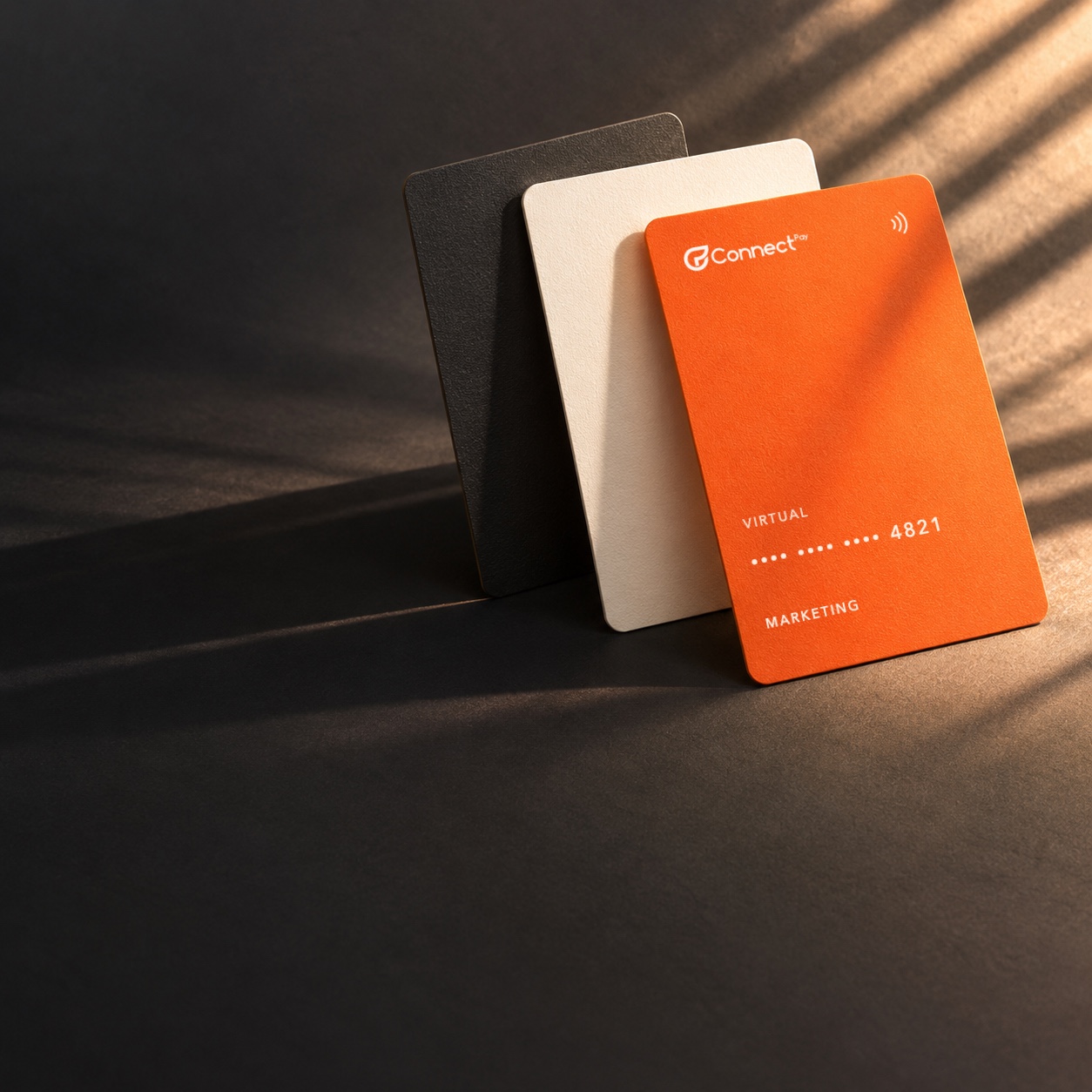 Três cartões apoiados em pé sobre papel grafite; o da frente, laranja, com a marca ConnectPay e final 4821