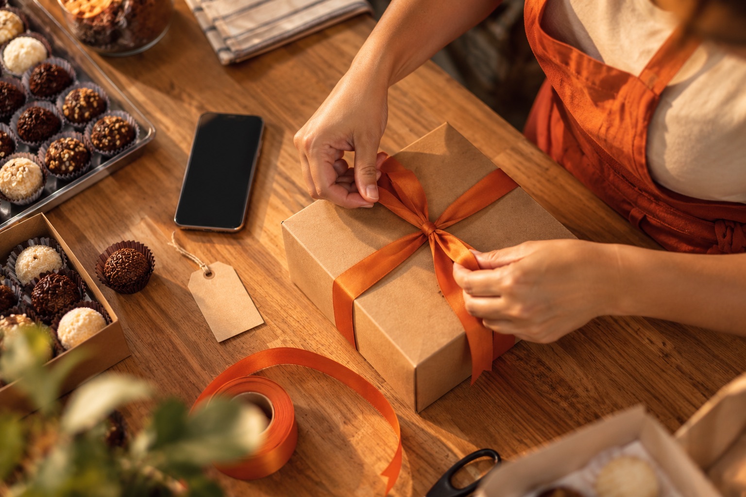 Mãos fechando uma caixa de encomenda ao lado do celular